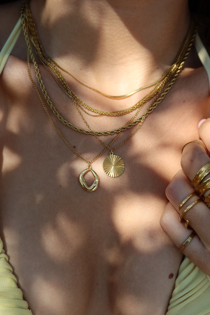Close-up of a person wearing gold necklaces and rings on a blurred natural background