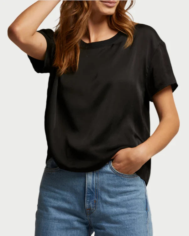 A person in a Delphine Satin Crewneck Tee by perfect white tee and blue jeans stands with one hand on their hip, the other arm raised, slightly tilting their head. The outfit is an elevated essential, blending casual style with sophistication.