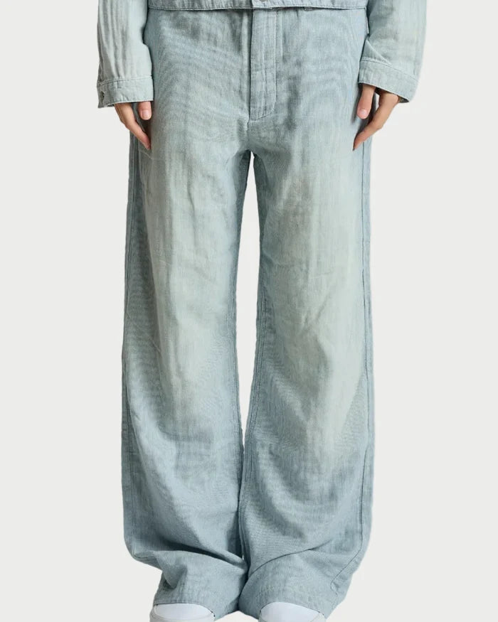 A person wearing light blue wide-leg denim pants with a matching light blue cropped jacket and white sneakers, shown from the chest down against a plain light gray studio background.