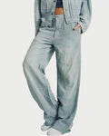 A person wearing light-wash wide-leg denim pants with a matching cropped denim jacket and white sneakers, standing against a plain light gray studio background.