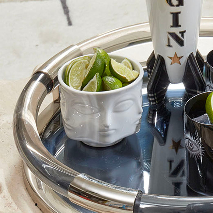 Silver tray with a bowl of limes, a bottle of gin, and a glass on a marble surface.