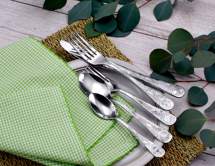 Top view of Earth flatware showing engraved handles on forks and spoons with green gingham napkin and eucalyptus