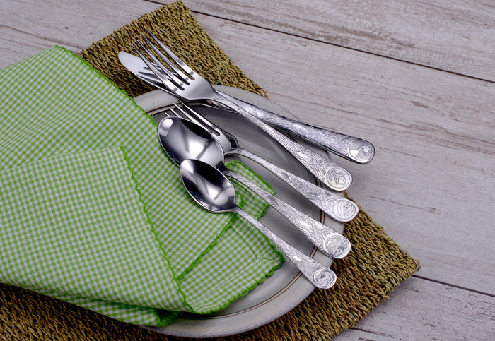Forks, knives and spoons stacked on a plate with a green gingham napkin on a woven placemat