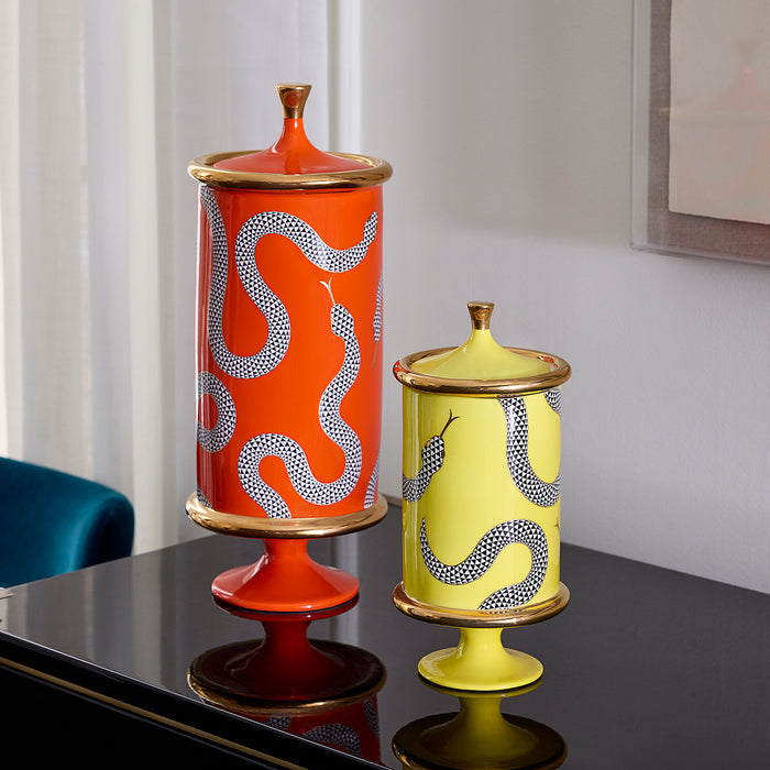 Two decorative ceramic lidded vases with snake motifs, one orange and one pale yellow, displayed on a glossy black table in an indoor setting.