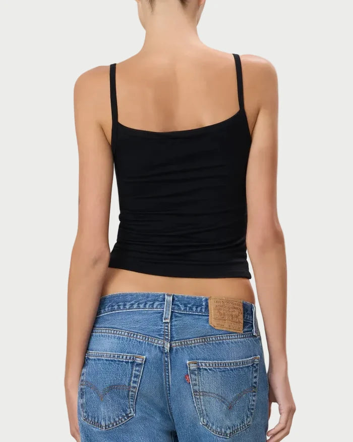 Person wearing a black tank top and blue jeans on a light gray background