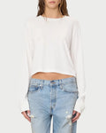 A woman wears the Éterne Long Sleeve Boxy Tee by Eterne, featuring a relaxed boxy fit in a soft cotton-modal blend, paired with light blue ripped jeans and standing against a plain background.