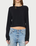 A person is standing against a plain background wearing the Éterne Long Sleeve Boxy Tee by Eterne in a soft cotton-modal blend, paired with light blue ripped jeans. Their look is highlighted by a black cropped silhouette top, and their hair appears wet with their face partially out of frame.