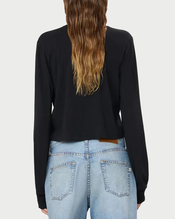 A person with long, wavy brown hair is shown from the back against a plain, light background, wearing the Éterne Long Sleeve Boxy Tee by Eterne in black—a soft cotton-modal blend—paired with light blue jeans.