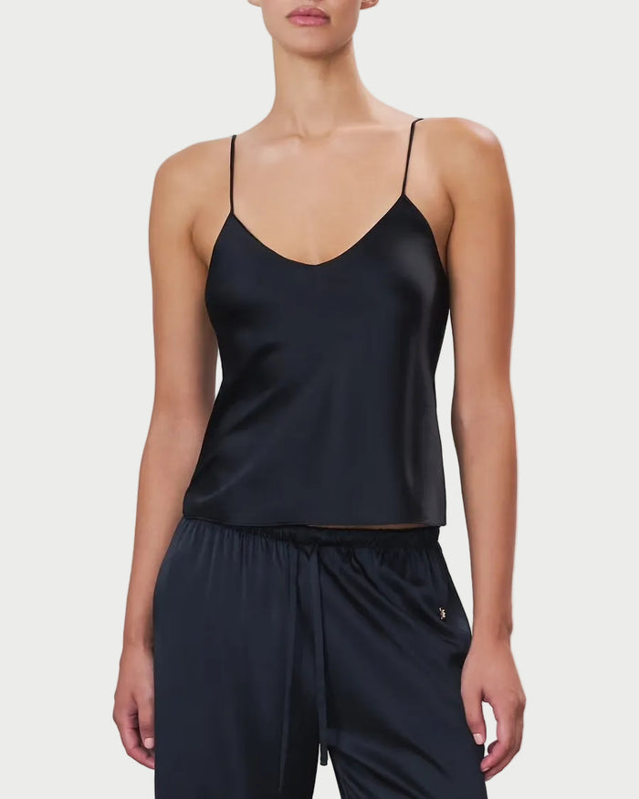 Woman wearing a black satin camisole and pants on a light gray background
