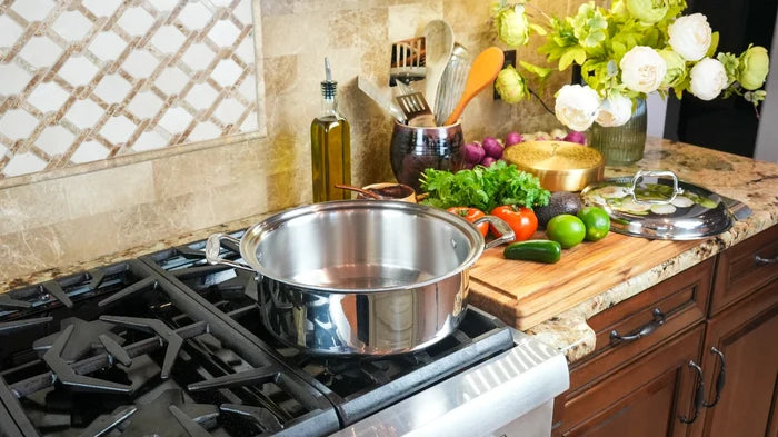 Stainless steel 6‑quart stockpot on a gas stove with lid and vegetables on a cutting board nearby