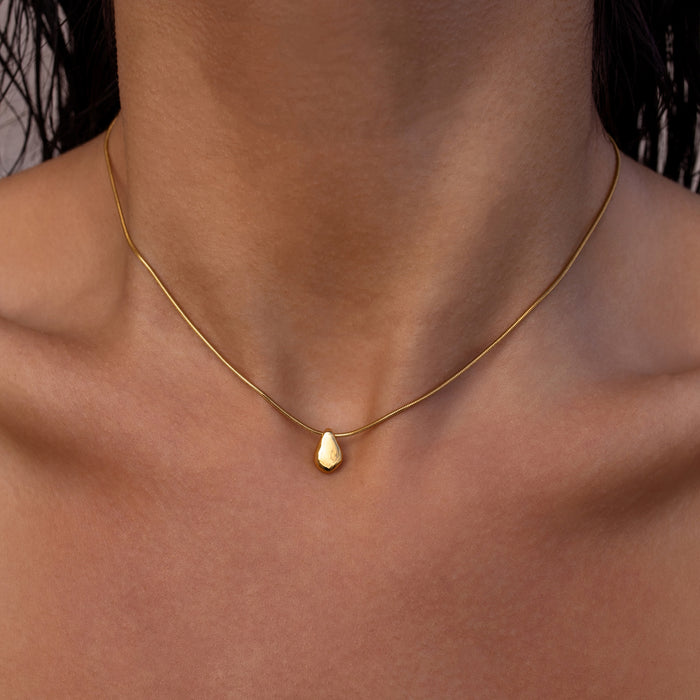 Dainty gold necklace with a gold teardrop pendant on a person's neck