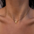 Dainty gold necklace with a gold teardrop pendant on a person's neck