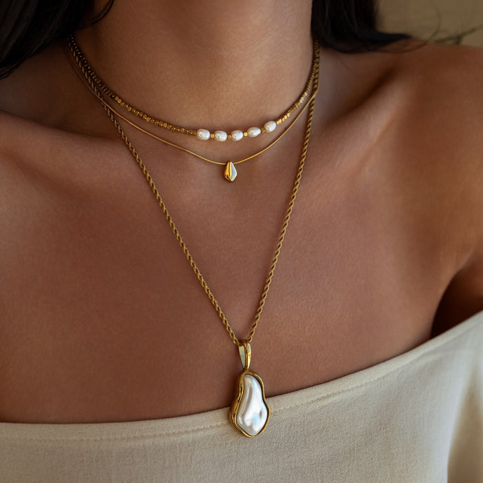 Close-up of a person wearing three gold necklaces with pearl pendants.