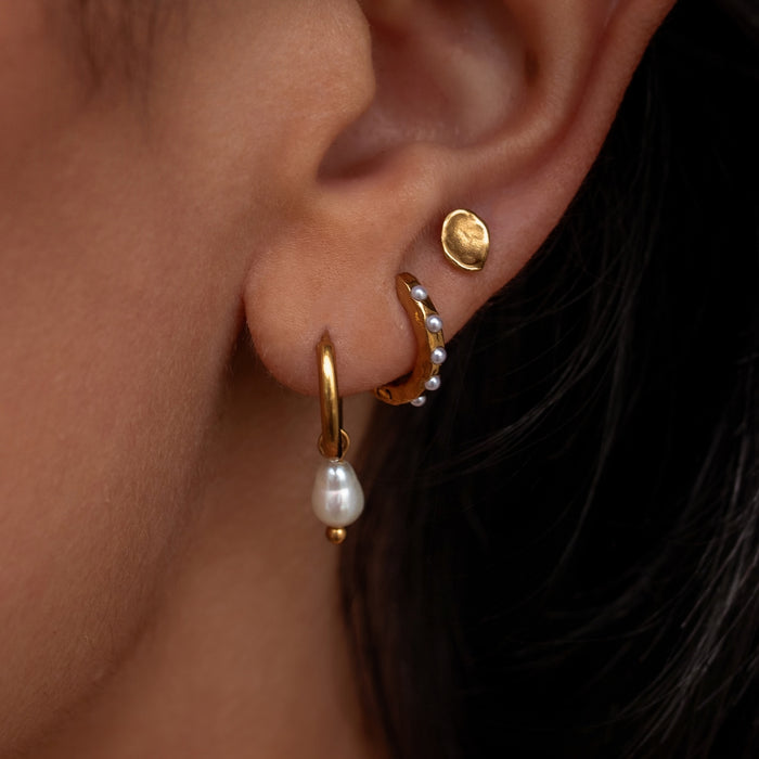 Close-up of an ear wearing gold hoop earrings with pearl accents.