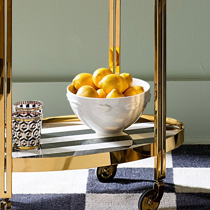 Gold bar cart with a bowl of lemons and a glass on a checkered floor.
