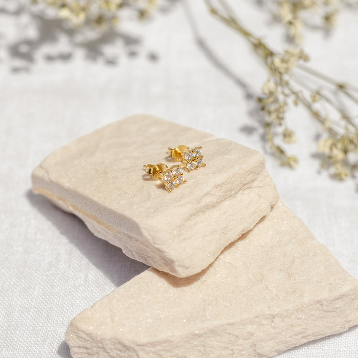a flat lay image of dainty gemstone earrings with four diamonds each on a neutral background
