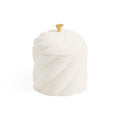 A white ceramic lidded container with a sculpted, twisted spiral design and a small gold-toned knob on top, set against a plain white background.