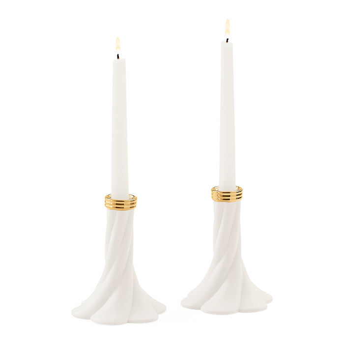 Two white taper candles in sculptural flared holders with gold bands, shown on a plain white background.