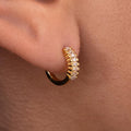 A close-up image of a gold-plated huggie earring with cubic zirconia stones on a person's ear.