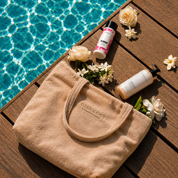 Sac de plage beige Gemology au bord d'une piscine avec soins cosmétiques et fleurs blanches