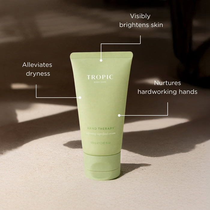 Tropic Hand Therapy softening superfood cream tube in sage green, annotated with three benefits: visibly brightens skin, alleviates dryness, and nurtures hardworking hands.