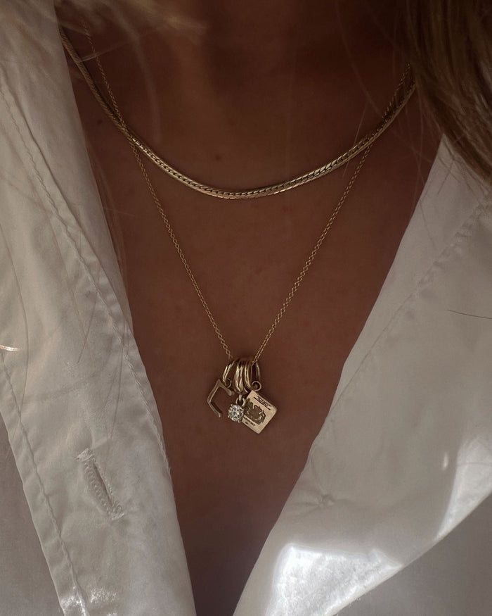 woman wearing a 14k Gold Hangul Korean Alphabet Charm in D with a MileStone Drop Charm and Passport Charm hanging from a chain necklace