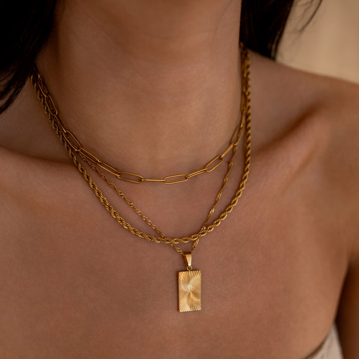 Close-up of a person wearing three gold necklaces with a rectangular pendant.