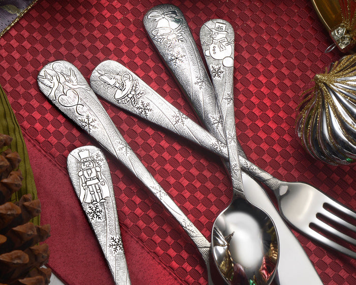 Top-down view of Holidays flatware with engraved festive handles on a red textured placemat and gold ornament