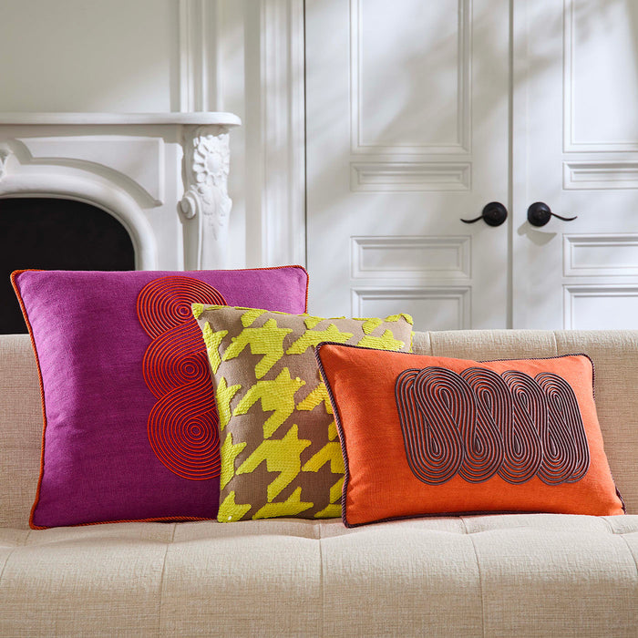 Three colorful pillows on a beige sofa with a white wall and fireplace in the background.