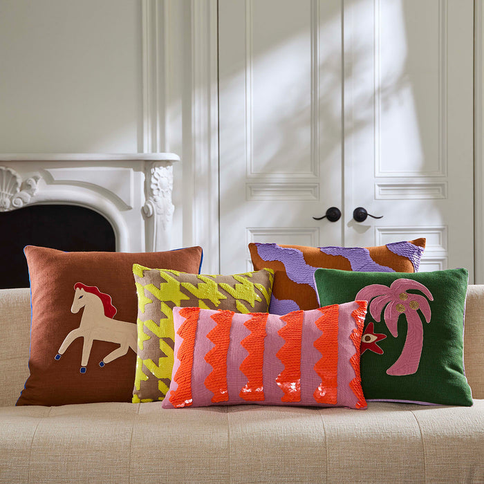 Colorful pillows with various designs on a beige sofa in a room with white paneled walls.