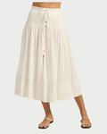 A woman wears the Ilio Nema Diana Skirt, crafted from organic white voile with subtle stitching, a tie waist, and button-front details. Its relaxed fit and flowy silhouette from Ilio Nema pair effortlessly with flat sandals for elegant ease.