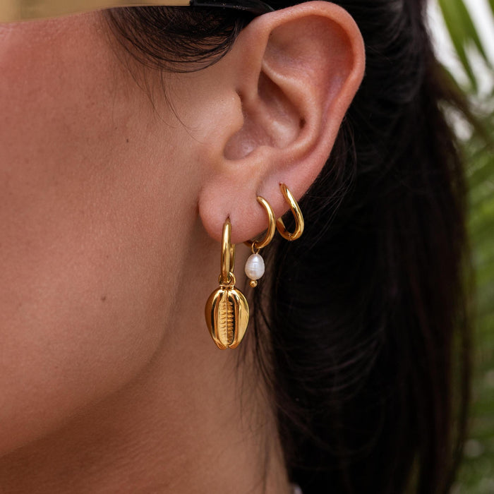 a fun vacation earring stack featuring puka shell huggies, dainty pearl huggies, and simple gold huggies