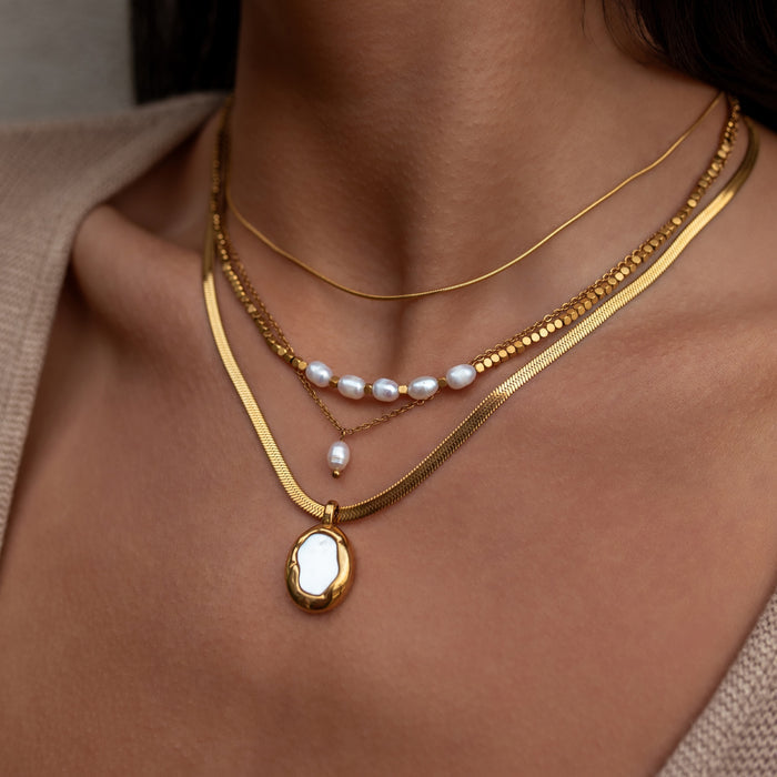 Close-up of a person wearing multiple gold necklaces with pearls.