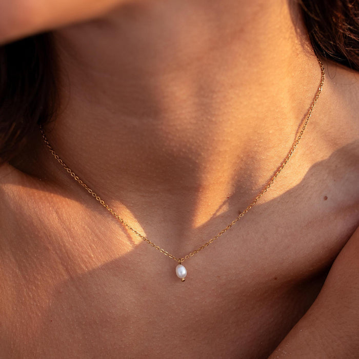 a dainty gold necklace with a single freshwater pearl pendant