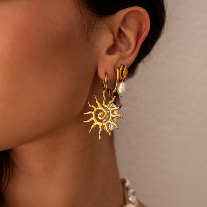 Gold sun-shaped earring with pearl earrings stacked behind it