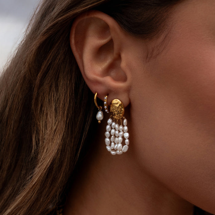 Close-up of a woman's ear wearing gold and pearl earrings.
