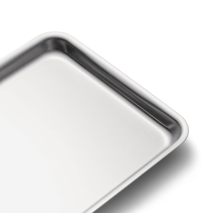 Angled close up top view of stainless steel jelly roll pan showcasing rolled edges and shallow rounded corners on white background