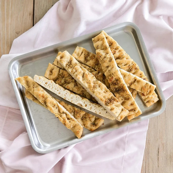 Top view of stainless steel jelly roll pan showing raised lip and brushed finish with herb-seasoned focaccia on a pink cloth