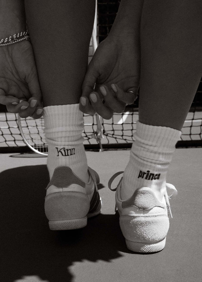 Black and white photo of a woman wearing Kinn x Prince Crew Socks on a tennis court