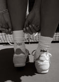 Black and white photo of a woman wearing Kinn x Prince Crew Socks on a tennis court