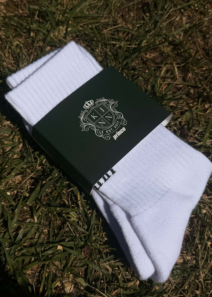 A pair of packaged Kinn x Prince Crew Socks laying on the grass