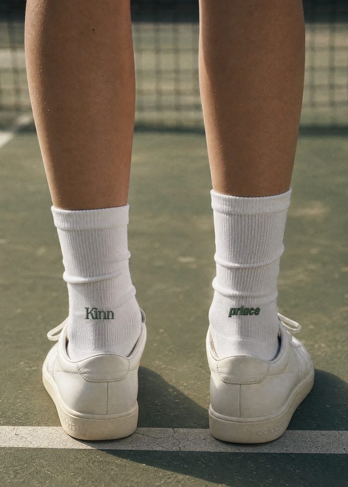 Back of the legs of a woman on a tennis court wearing Kinn x Prince Crew Socks