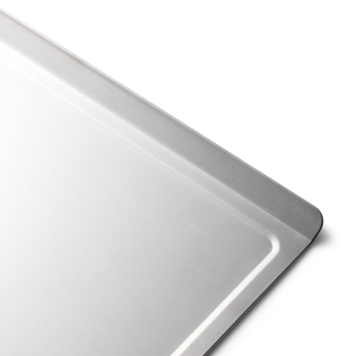 Corner of a stainless-steel baking sheet with rolled rim and flat interior surface.