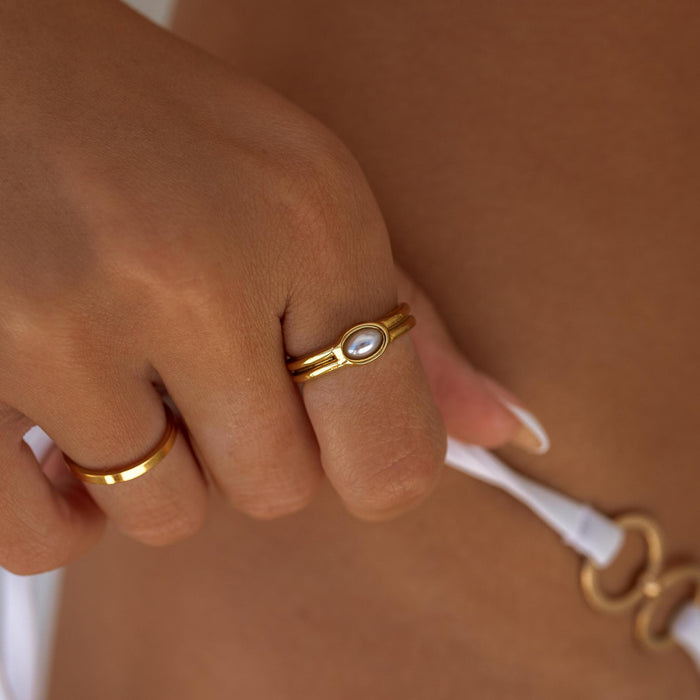 Close-up of a hand wearing dainty gold and pearl rings with a blurred background.