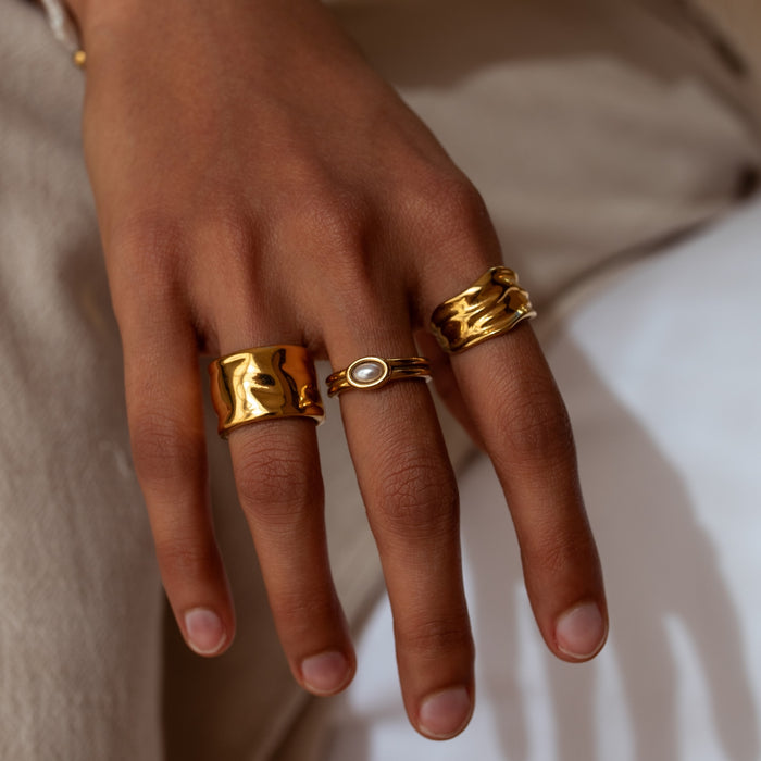 Hand wearing three gold rings on a neutral background