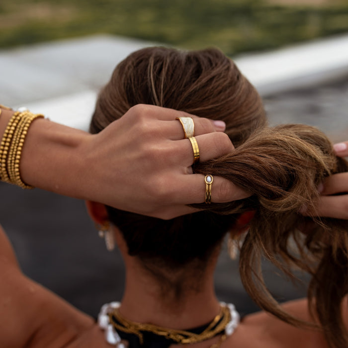 Person adjusting their hair with jewelry, blurred natural background