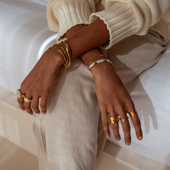 Close-up of a person's hands wearing gold and pearl jewelry on a neutral background