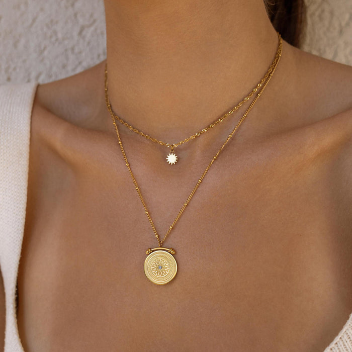 Gold double layer necklace with pendants on a person's neck against a neutral background