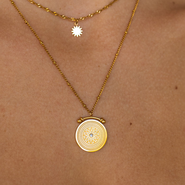 close up of gold coin pendant with unique detailed designs and a small gemstone in the center