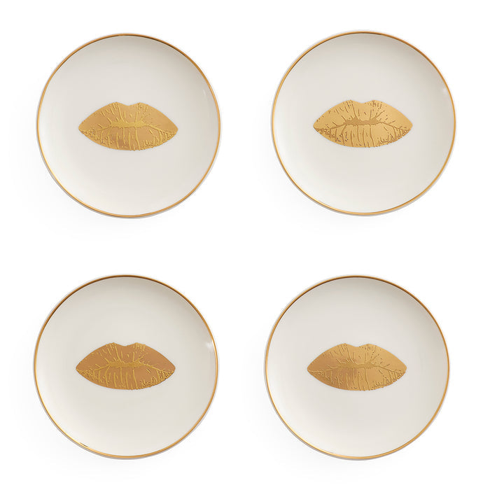 Four round white plates arranged in a 2x2 grid on a white background, each with a thin gold rim and a gold lips motif centered on the plate.